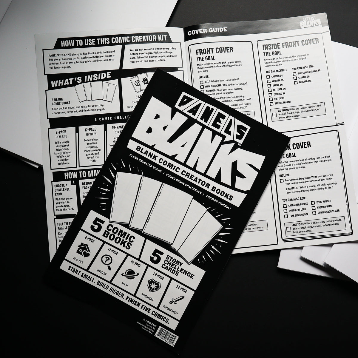 A tabletop flat-lay of the 'PANELS Banks' comic creator board kit, showing the black-and-white instruction booklet in the foreground surrounded by white paper sheets on a dark surface.