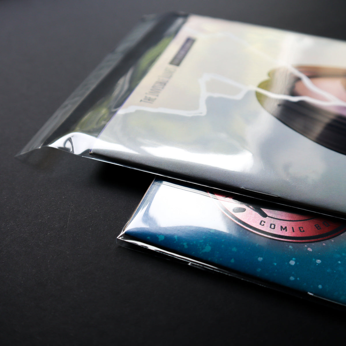 Two sealed comic books on a dark surface. 
