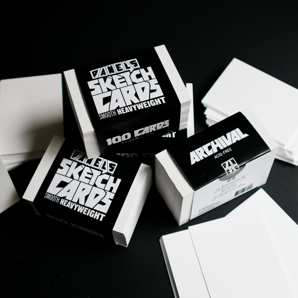 Several stacks of white sketch cards and their black-and-white boxes are arranged on a dark black background. The boxes read 'PANELS SKETCH CARDS' and 'ARCHIVAL SKETCH CARDS' with '100 CARDS' visible.