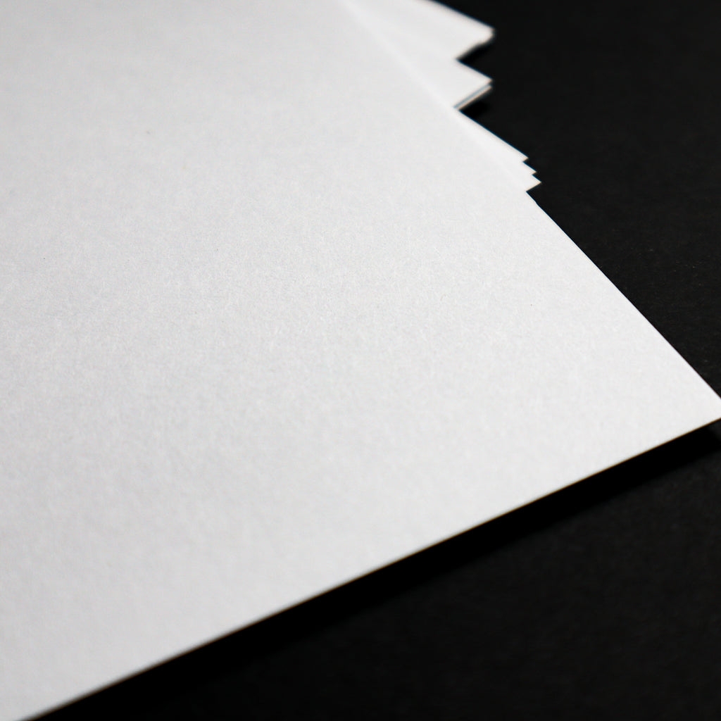 A close-up of a stack of white textured paper sheets fanned out against a solid black background.