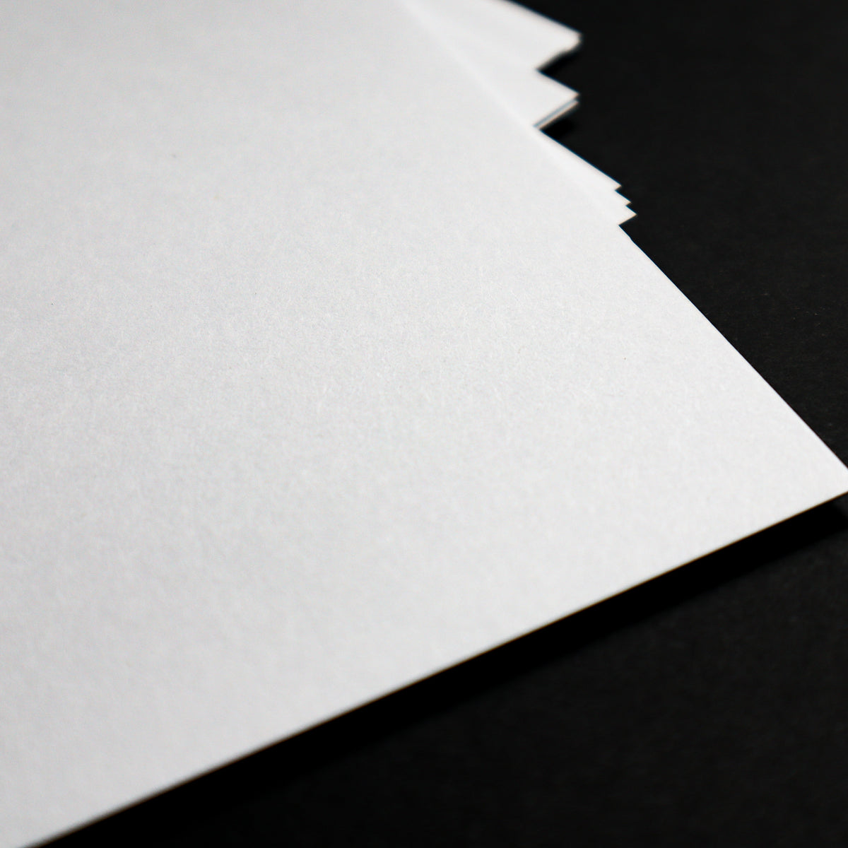A close-up of a stack of white textured paper sheets fanned out against a solid black background.