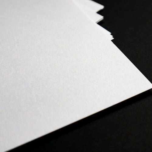 A close-up of a stack of white textured paper sheets fanned out against a solid black background.
